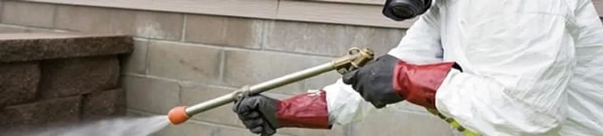 Pest control technician applying exterior insect treatment along a home foundation in Orange, CA