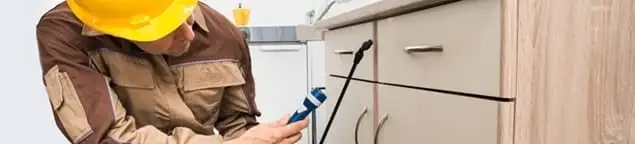 Roach exterminator applying treatment under kitchen cabinets in Orange, CA