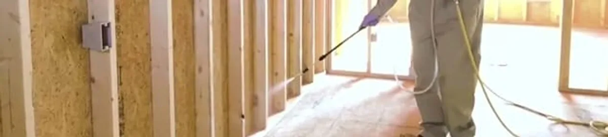 Termite treatment technician applying spray along framing and unfinished walls in Orange, CA