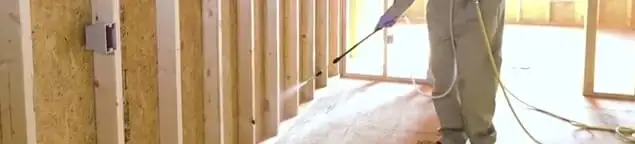 Termite treatment technician applying spray along framing and unfinished walls in Orange, CA